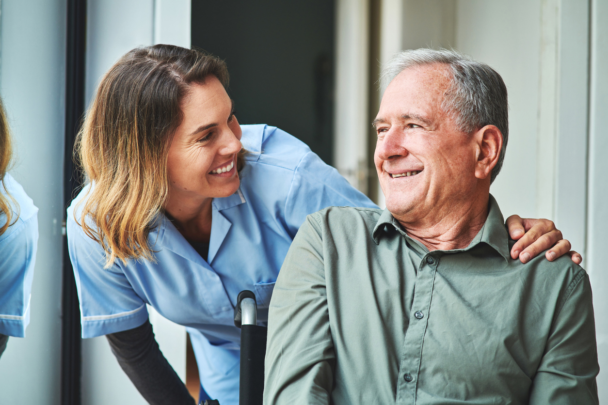 An elderly man laughing with a young female caregiver in blue scrubs