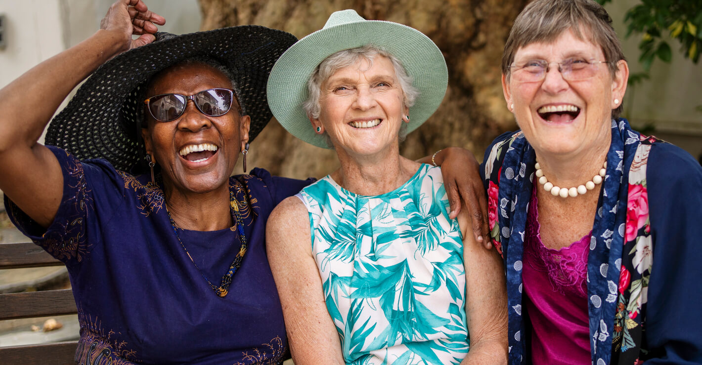 Three laughing senior women sitting on a bench